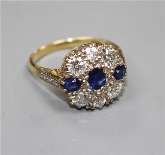 A Victorian style 18ct, three stone sapphire and six stone diamond set circular cluster ring, with diamond set shoulders,
